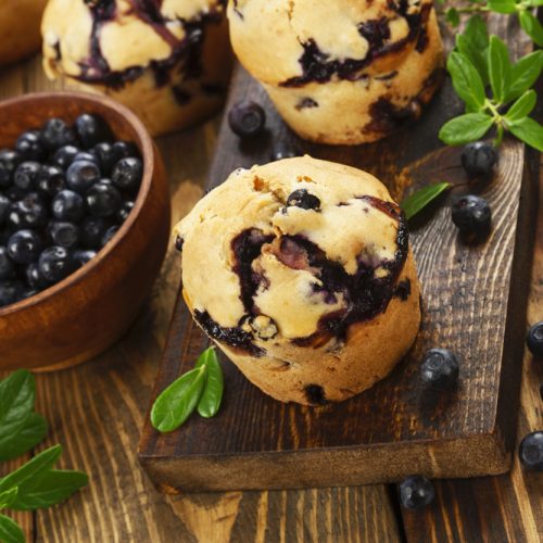 Blueberry muffins on a wooden tabletop next to a small bowl of blueberries
