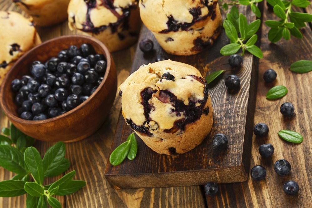 Blueberry muffins on a wooden tabletop next to a small bowl of blueberries