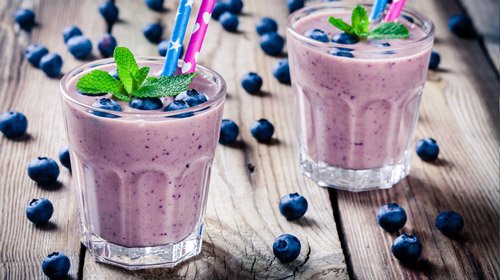 Blueberry smoothie in a short glass with two straws